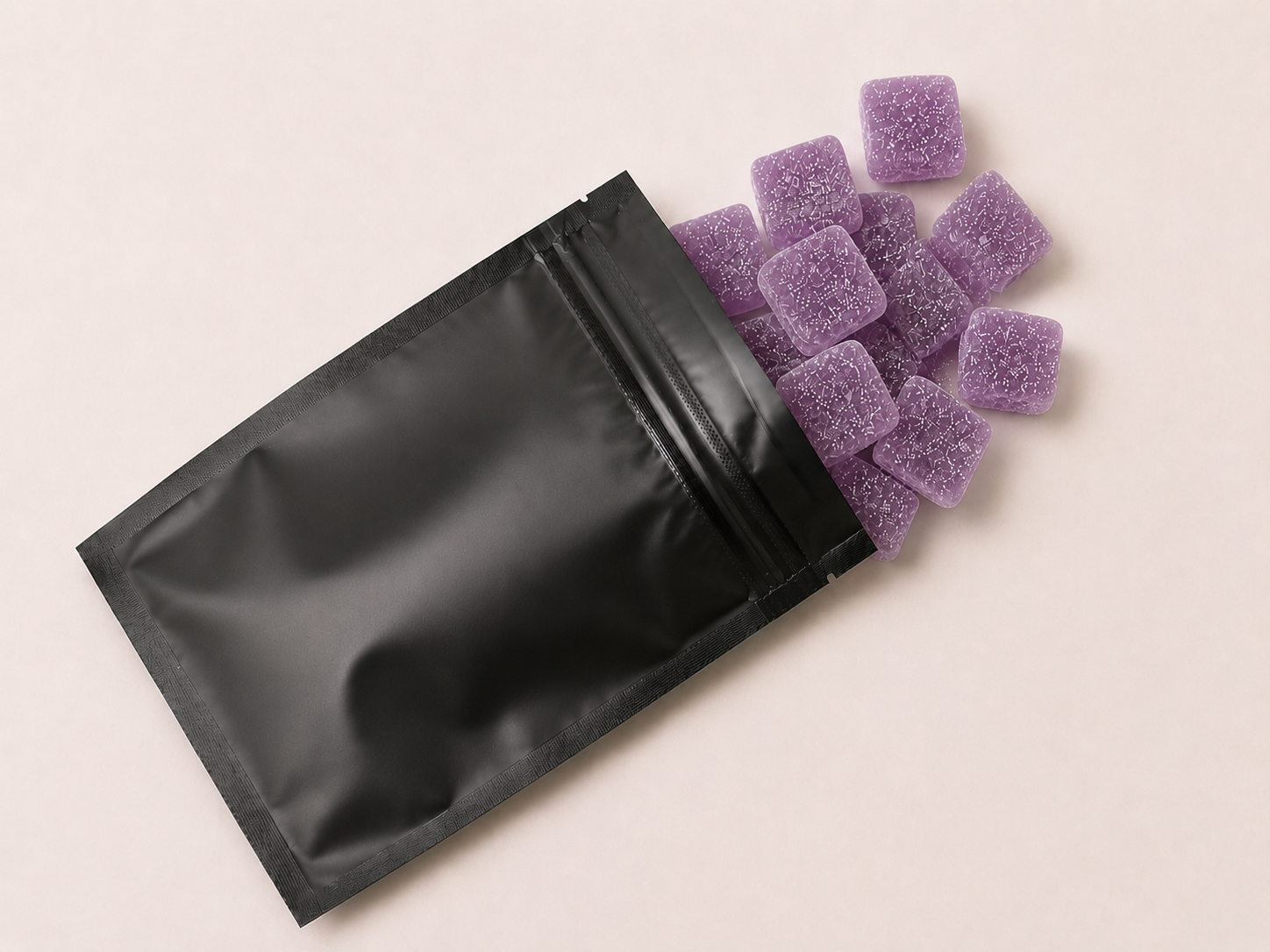 Purple sugar-coated gummy squares spilling from a black pouch